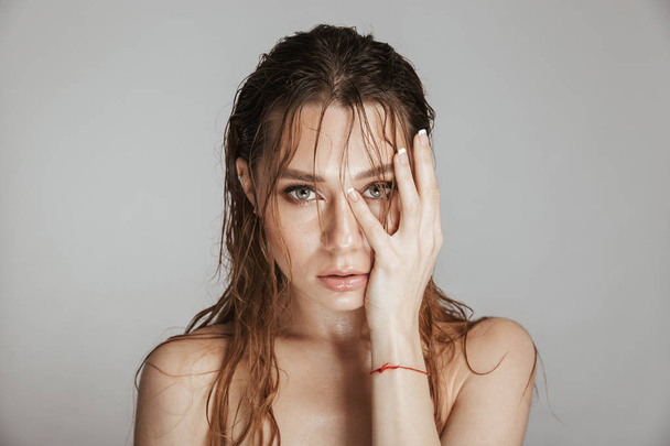 Fashion portrait of a topless attractive woman with makeup and wet hair posing isolated over gray background - Fotó, kép