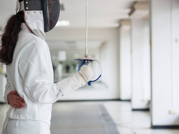 Close-up of a fencer in white fencing suit and holding a sword on gym background.sport concept. - Zdjęcie, obraz
