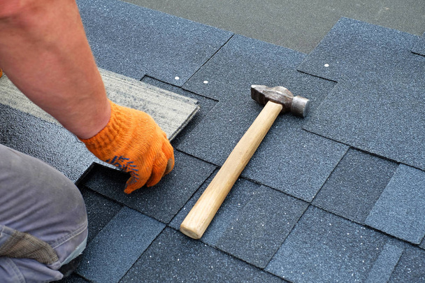 Bauunternehmer verlegt Bitumen-Dachschindeln mit Hammer in Nägeln. - Foto, Bild