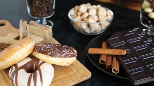 Tumma suklaa kanelitikkuja lautasella vieressä donitseja ja vohveleita puulaudalla
 - Materiaali, video