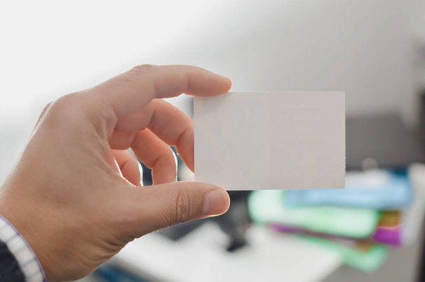 Closeup image of holding business card, person hand showing plain mock up space on professional office background. Businessman communication information - 写真・画像