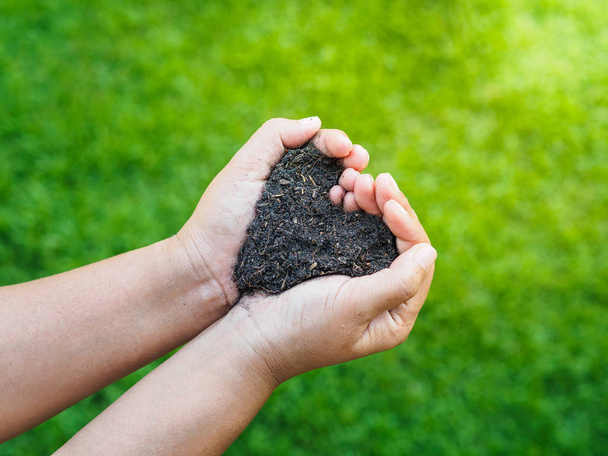 Eart day, save the earth, love concept. the woman hand holding a soil on green grass blur background. - Photo, Image