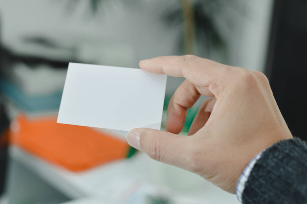 Closeup image of holding business card, person hand showing plain mock up space on professional office background. Businessman communication information - 写真・画像