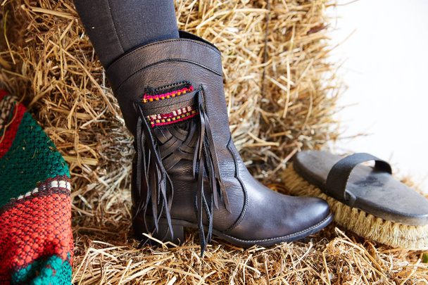 female black boot on stable straw bale with horse brush - Фото, зображення