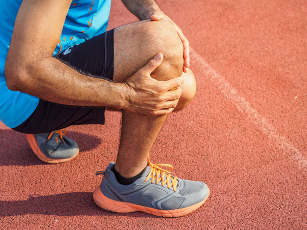 Knieverletzungen. Sportmann mit kräftigen athletischen Beinen, der das Knie mit schmerzenden Händen hält, nachdem er sich beim Lauftraining auf der Laufstrecke eine Muskelverletzung zugezogen hat. Gesundheits- und Sportkonzept. - Foto, Bild
