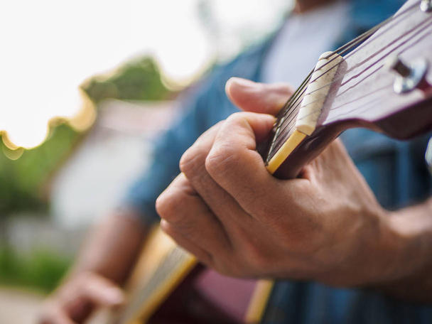 guapo músico tocando la guitarra acústica sobre fondo borroso. concepto de música e instrumento
. - Foto, Imagen