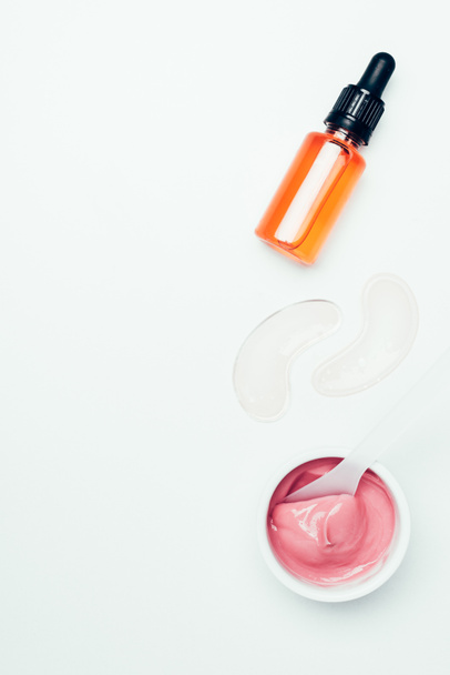 top view of cosmetic bottle with pipe, eye patches, spoon and pink mask in container isolated on white  - Photo, Image