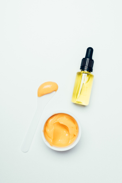 top view of cosmetic bottle with pipe, spoon and orange mask in container isolated on white surface - Фото, зображення