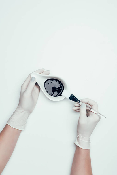 cropped shot of woman in latex gloves holding black mask and brush isolated on white surface  - Photo, image