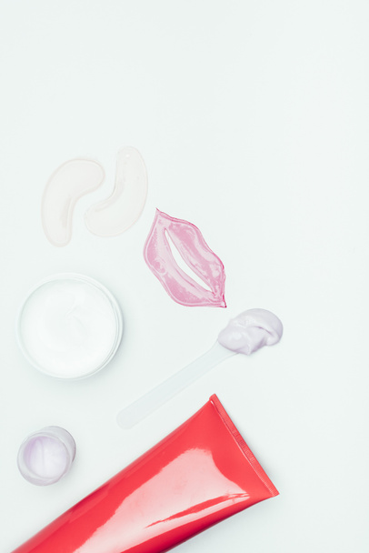 bovenaanzicht van lip masker, ogen patches, klei masker in container en crème fles geïsoleerd op wit oppervlak  - Foto, afbeelding