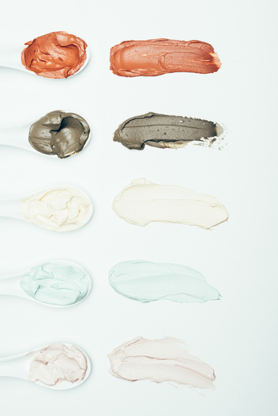 kaşık ve beyaz yüzey üzerinde izole satır yerleştirilen çeşitli renkli kil maskesi lekeler üstten görünüm  - Fotoğraf, Görsel