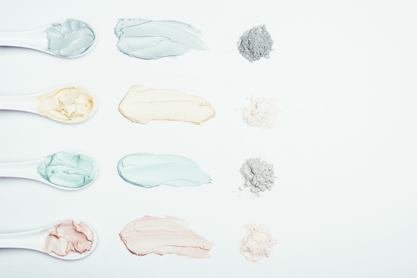 flat lay with spoons, clay powder and colorful clay mask smudges placed in row on white surface  - Foto, Imagem