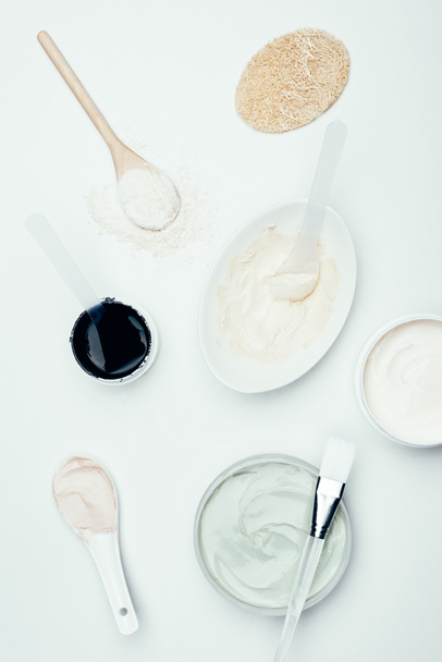 flat lay with sponge, various clay masks in containers, plate, clay powder, spoons and brush isolated on white surface  - 写真・画像