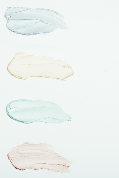 επίπεδη lay με τέσσερις πολύχρωμο άργιλος μάσκα μουτζούρες τοποθετούνται σε σειρά που απομονώνονται σε λευκή επιφάνεια  - Φωτογραφία, εικόνα