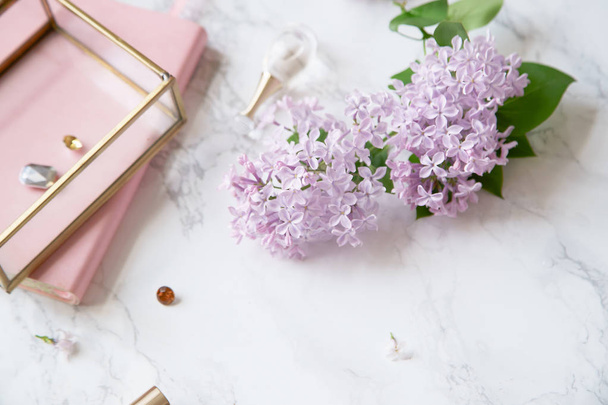 feminine workspace mock-up with lilac flowers and pink accessories on marble background - Fotó, kép