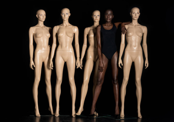 full length view of beautiful young african american woman in swimsuit standing between mannequins and looking at camera on black  - Φωτογραφία, εικόνα