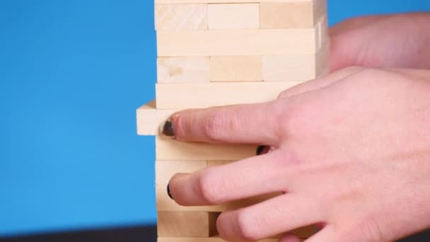 Womans hands playing boardgame Jenga. blue background - Felvétel, videó