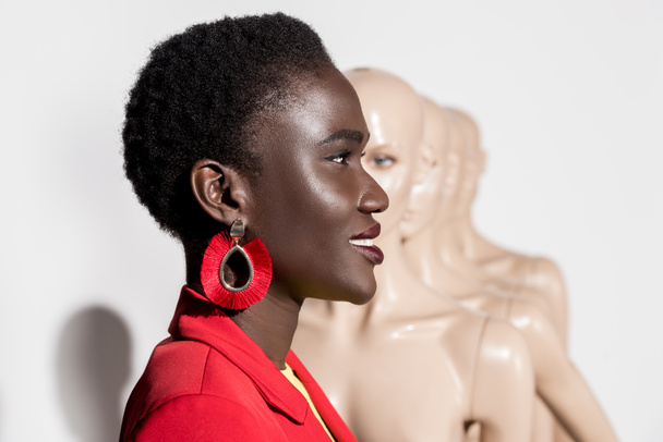 side view of beautiful smiling african american girl looking away and mannequins on white  - Фото, зображення