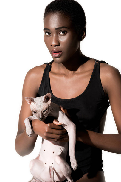 krásná mladá africká americká žena v plavkách hospodářství kočka a při pohledu na fotoaparát izolované na bílém - Fotografie, Obrázek
