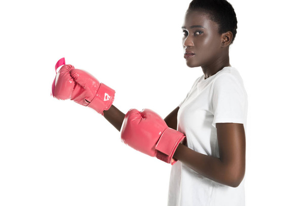 side view of african american woman in pink boxing gloves looking at camera isolated on white, breast cancer concept - Photo, Image