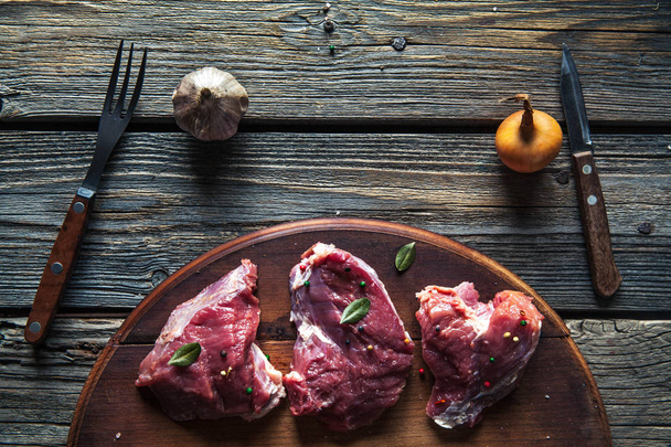Pieces of meat, steak with spices on a wooden background. Food - Фото, изображение