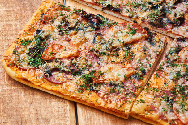 Cortar la pizza tradicional con champiñones, queso y tomates espolvoreados con hierbas en un plato de madera
 - Foto, Imagen