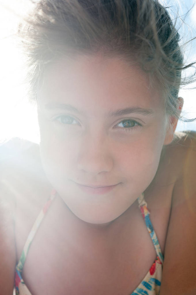 Baixo ângulo vista de belo sorriso sonhando menina closeup retrato em raios de luz solar. Imagem vertical vibrante de verão
. - Foto, Imagem