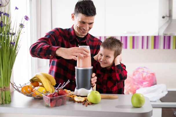 młody, wesoły ojca i syna w czerwone koszule gotowanie zdrowe śniadanie z blendera  - Zdjęcie, obraz