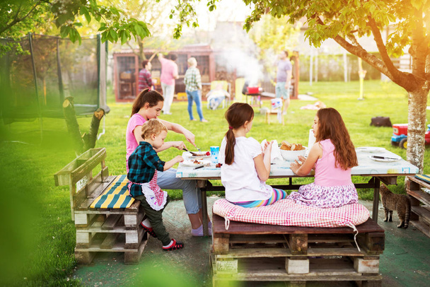 adorable children enjoying picnic sitting at table and eating grilled meat - Foto, immagini