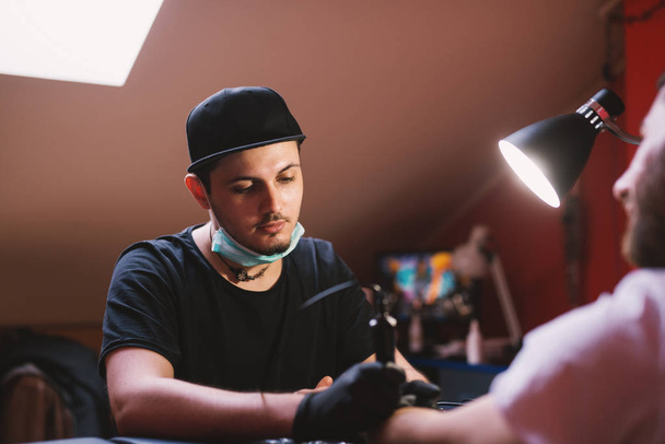 jonge gericht tatoeëerder inkt arm van klant - Foto, afbeelding