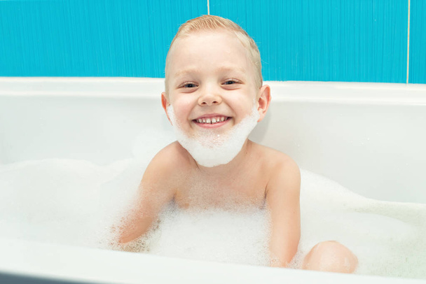 A little boy is playing with foam in the bathroom. - Foto, imagen