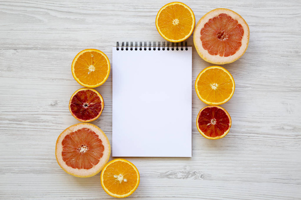 Citrus fruits (sicilian orange, grapefruit, orange) with notebook on white wooden background, from above. Flat lay. Top view. - Фото, изображение