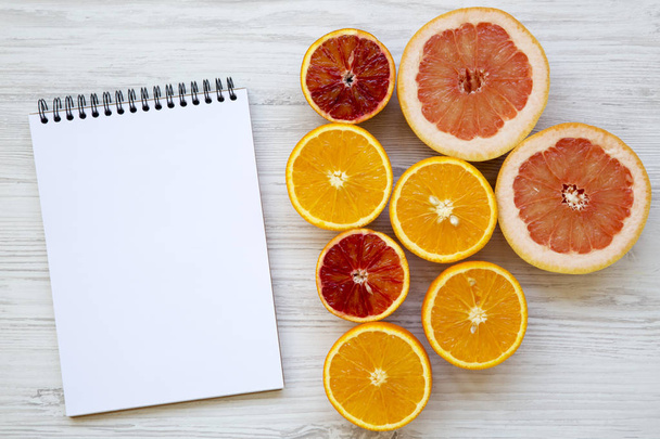 Citrus fruits (orange, grapefruit, sicilian orange) with blank notepad on white wooden background, from above. Flat lay. Top view. - Фото, изображение