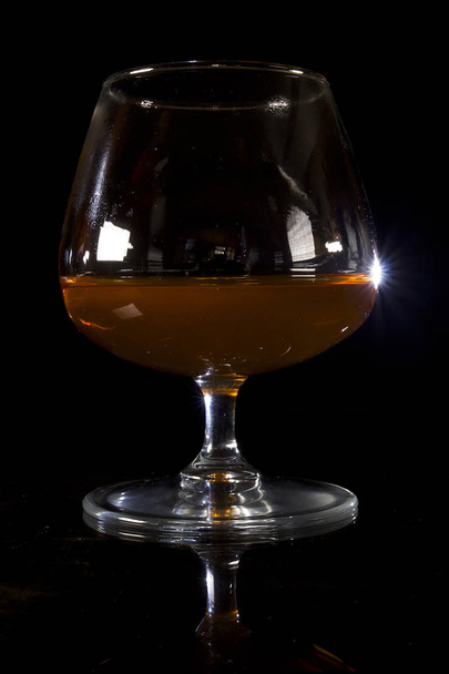 A glass of cognac on a black background on a reflective surface - Foto, Imagem