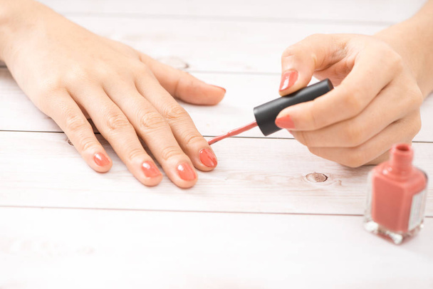 Kobiece ręce czerwony manicure i otwartą butelkę lakieru na stole - Zdjęcie, obraz