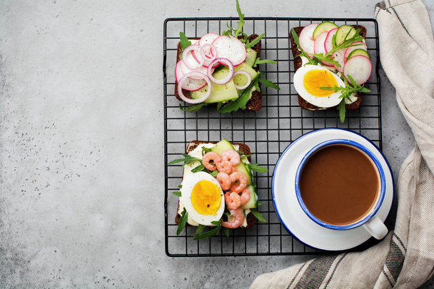 Open sandwiches on dark rye bread with eggs, shrimps, radishes, cucumber, cream cheese and arugula for breakfast. Smorrebrod Traditional dish of Danish cuisine. Top view. - 写真・画像