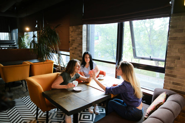 Νεαρό θηλυκό φίλους μιλώντας στο καφενείο και χρησιμοποιώντας το smartphone, πίνοντας τον καφέ. - Φωτογραφία, εικόνα
