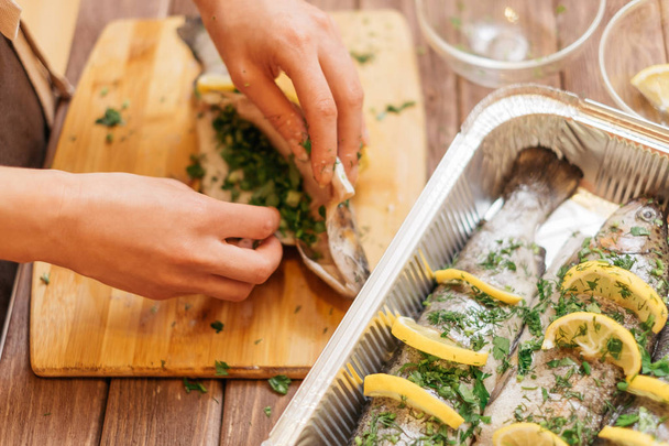 Female hands preparing fish trout with greenery on wooden board. - Foto, imagen