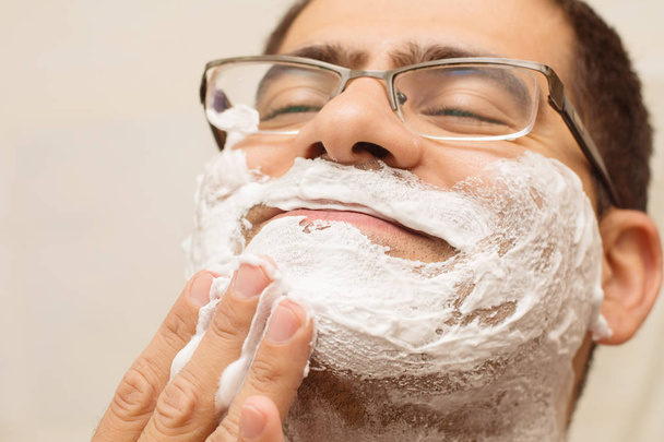 man in glasses Caucasian nationality shaves his face - 写真・画像