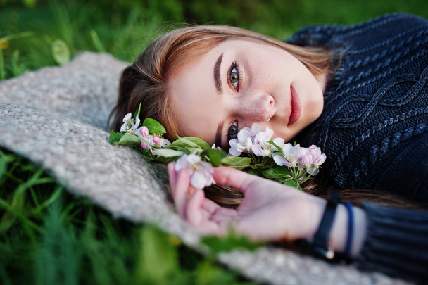 Young brunette girl lying on green grass with branches of blossom tree. - Foto, Bild