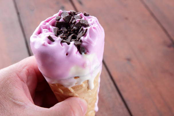 Ice cream cone with chocolate in hand. Ice cream on a dark wooden background. Cold milk dessert in a waffle cup in a man's hand. Summer cold dessert with copy space - Photo, Image