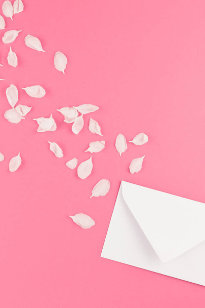 Piatto creativo accumulate vista dall'alto concetto di dileggiare lettera in bianco e fiori di melo petali su sfondo rosa pastello con lo spazio della copia in stile minimal, modello per il testo - Foto, immagini