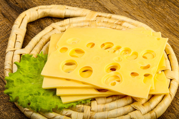 Близкий вид нарезанного сыра с листьями салата на деревянном фоне
 - Фото, изображение