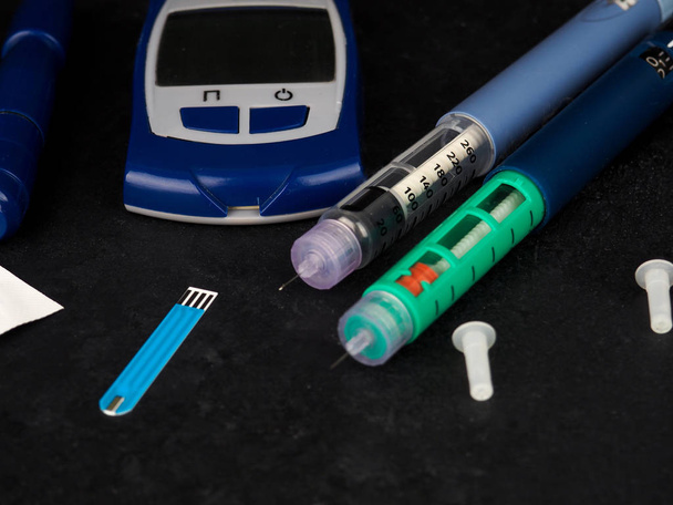 medicine, diabetes, advertisement and health care concept - close up of glucometer with blood sugar test stripe, insulin injection syringes and pills on table. - Photo, Image