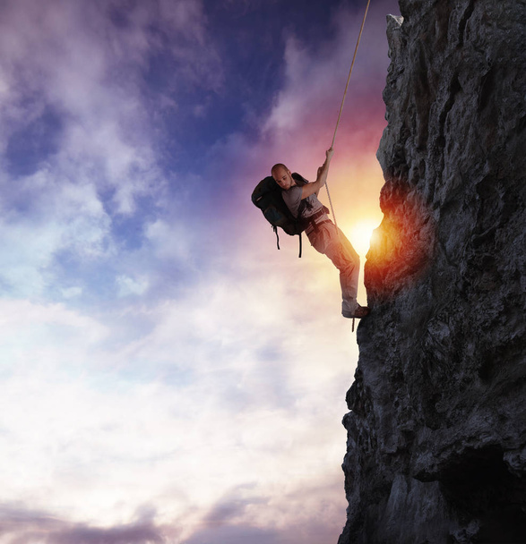 Homem sobe uma montanha de alto perigo com uma corda durante o pôr do sol
 - Foto, Imagem