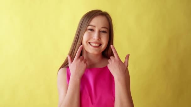 Close up of Young blonde woman smiles large to the camera, revealing white and perfect teeth on yellow background - Materiał filmowy, wideo