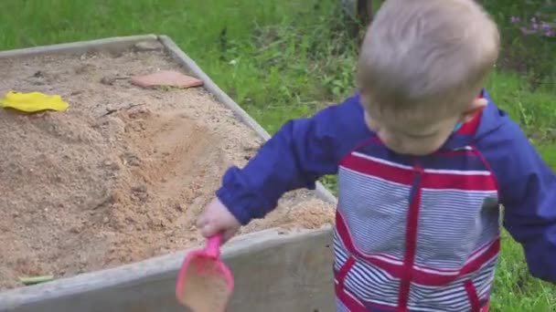 Pieni poika leikkii hiekkalaatikolla ja pyyhkii hiekkaa lenkkareista
. - Materiaali, video