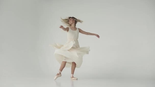 De ballerina is spinnen in dansen op spitzen in pointe-schoenen. balletdanseres in een licht wapperen jurk. aantrekkelijk meisje is dansen op een witte achtergrond - Video
