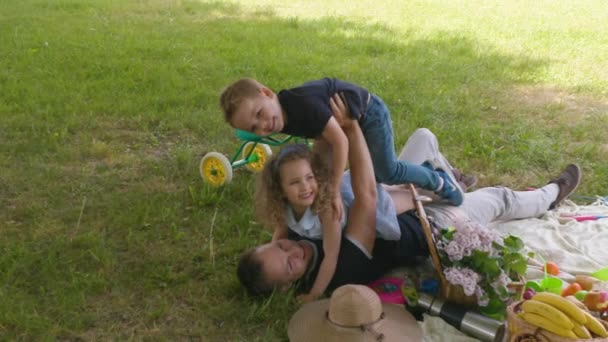 Dad rocks on the ground with his daughter and son in slow motion - Záběry, video