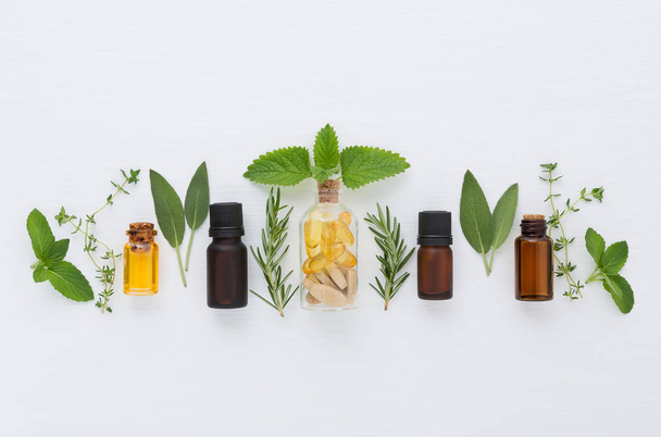 Bottle of essential oil and herbal medicine with fresh herbs sage, rosemary, thyme, mint, lemon balm and spearmint setup with flat lay on white wooden table. top view - Photo, Image